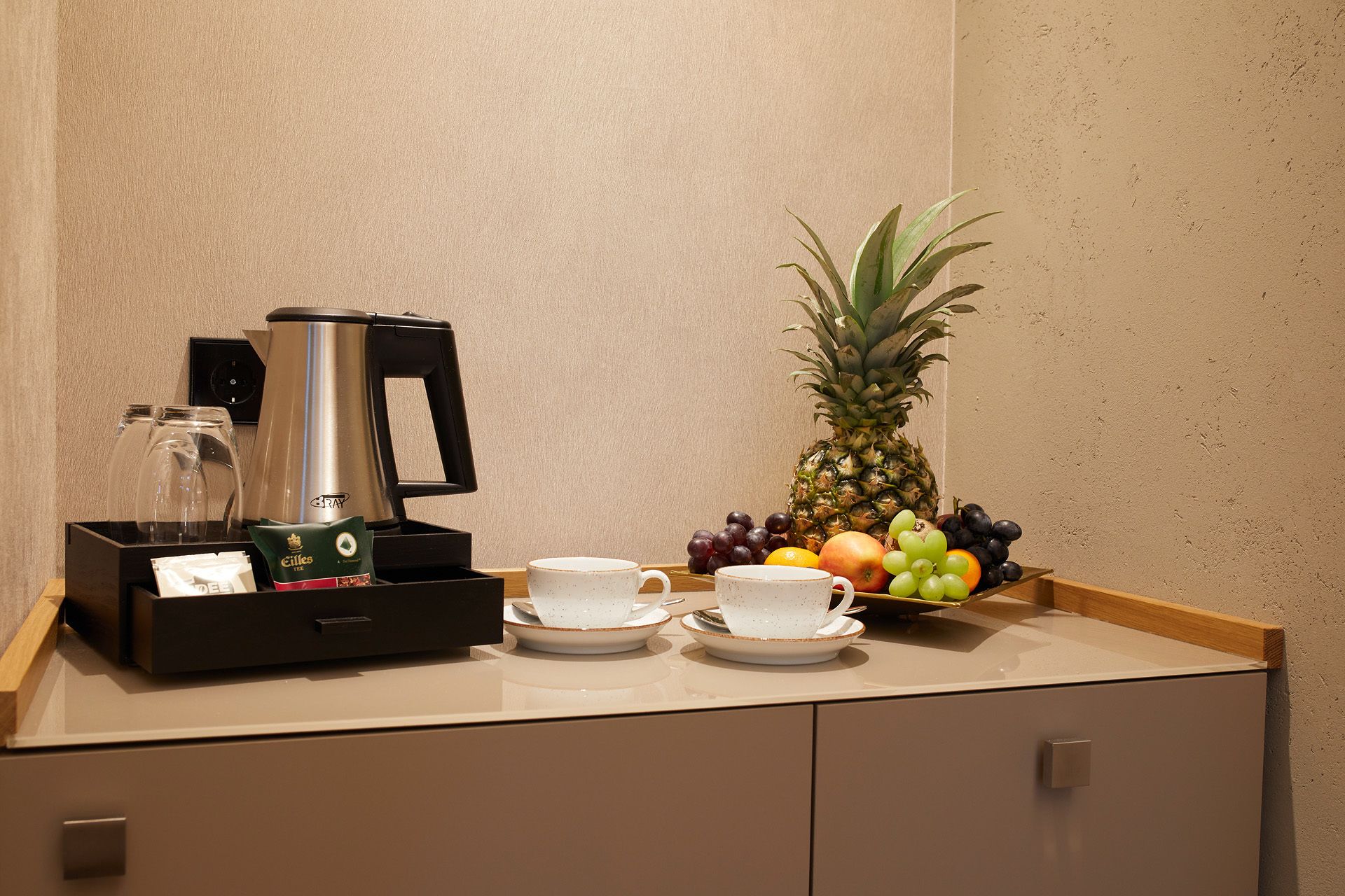 Una estación de café con cafetera, tazas y una bandeja de frutas.