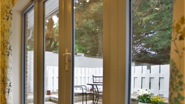 Una habitación con puerta de cristal corredera que da a un patio exterior con valla blanca, plantas en macetas y una mesa.