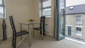 A small room with a glass table and two chairs, a window with blinds, and a view of a neighboring building. - Citystay Living - Dove House (Cambridge)