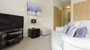 A modern living room with a flat-screen TV, a small side table, a white sofa, and a framed picture on the wall. - Citystay Living - Dove House (Cambridge)