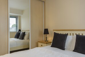 Een hotelkamer met een bed, een nachtkastje met een lamp, een spiegel en een raam met jaloezieën.