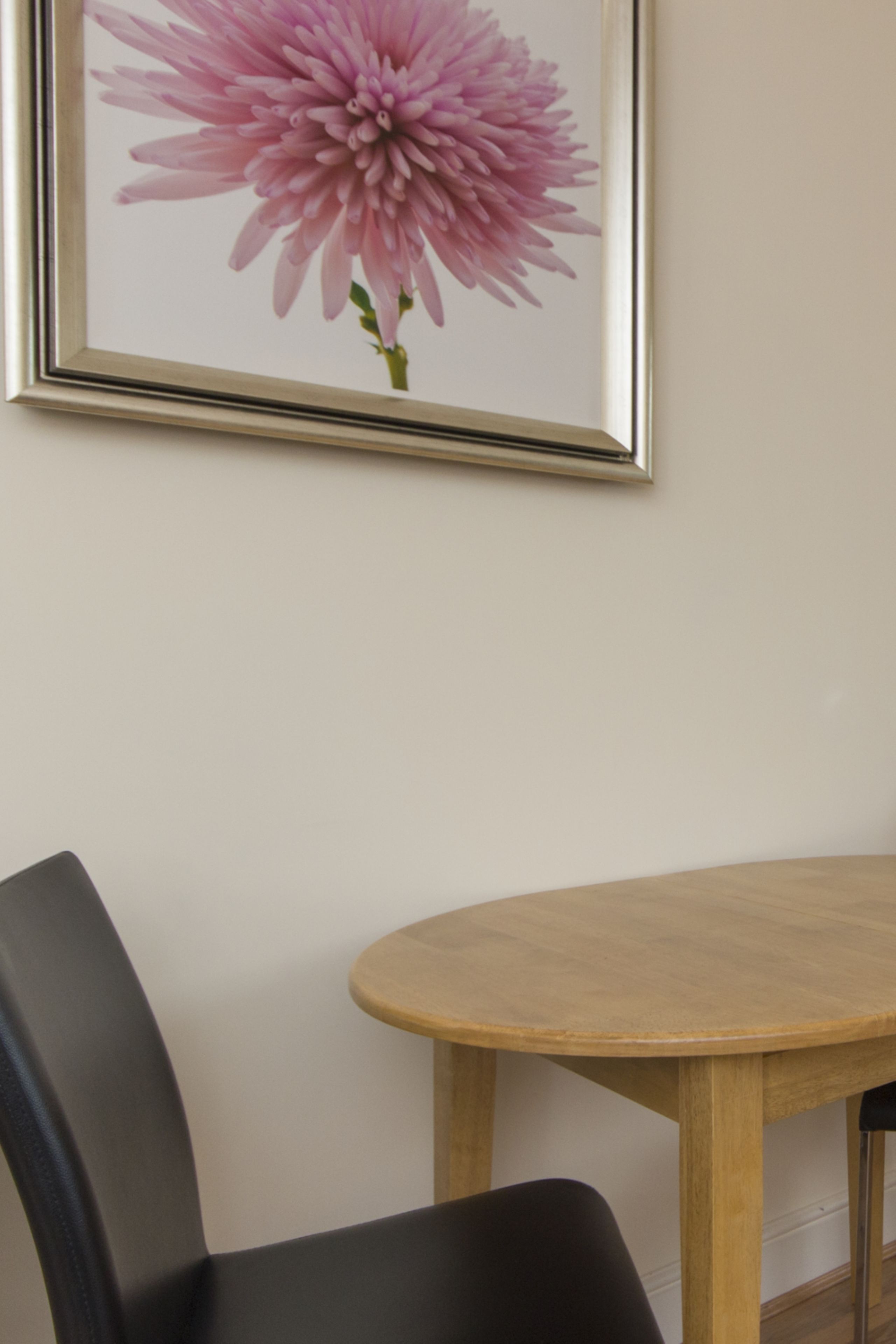 Een bloemig kunstwerk in een lijst aan de muur, een ronde houten tafel en een zwarte stoel.