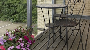 An outdoor seating area with a table and two chairs, a brick wall, and a hedge in the background. - Citystay Living - Citygate (Cambridge)