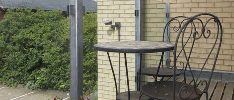 An outdoor seating area with a table and two chairs, a brick wall, and a hedge in the background.