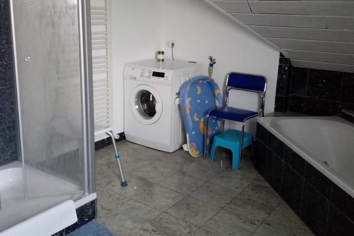 A small laundry room with a washing machine, a chair, and a bathtub.