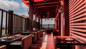 A restaurant with a red ceiling and wooden beams, featuring outdoor seating with tables and chairs. - Kegali Hotel (Accra)