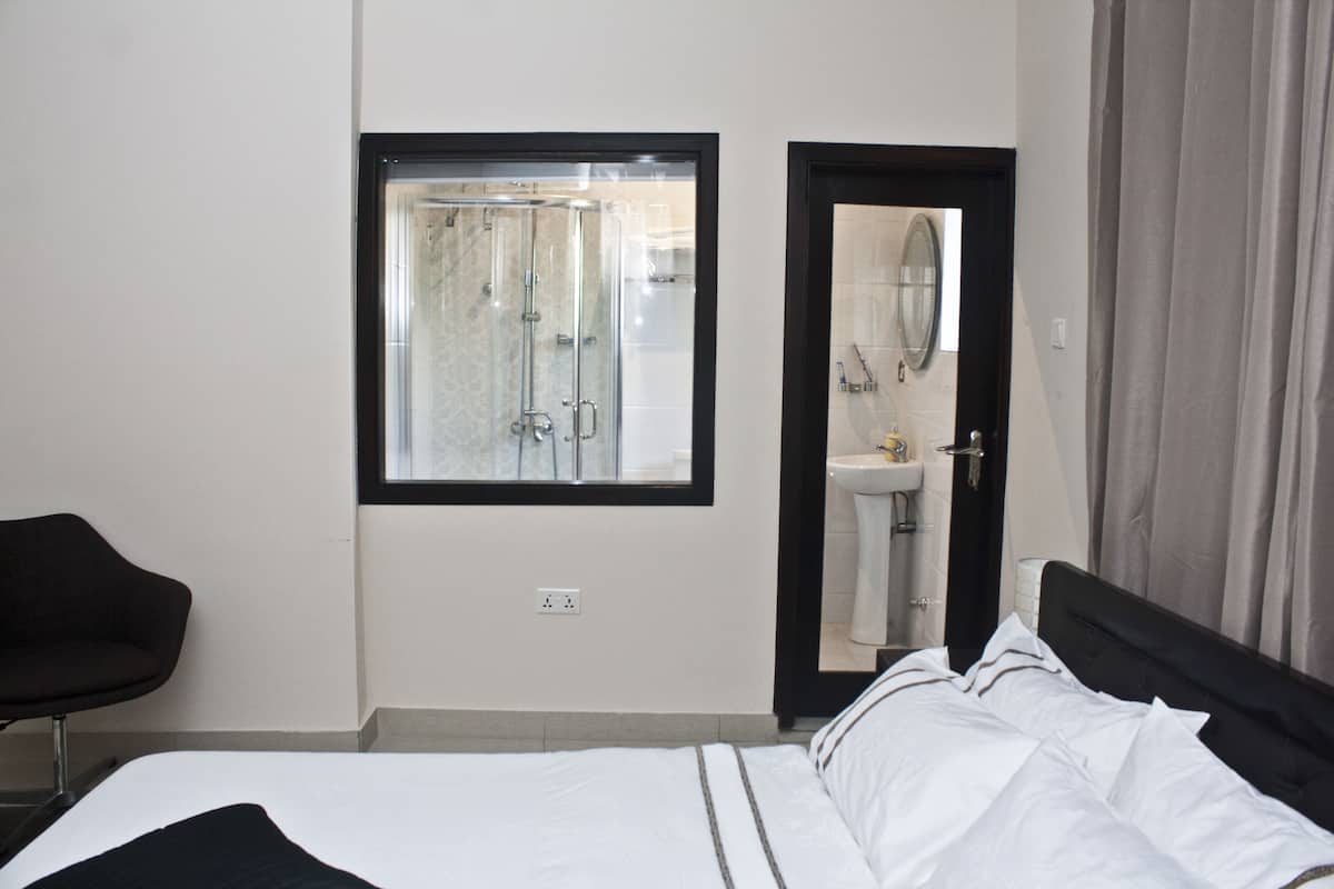 Habitación de hotel con cama, ventana con vista a una ducha, baño con lavabo y una silla.