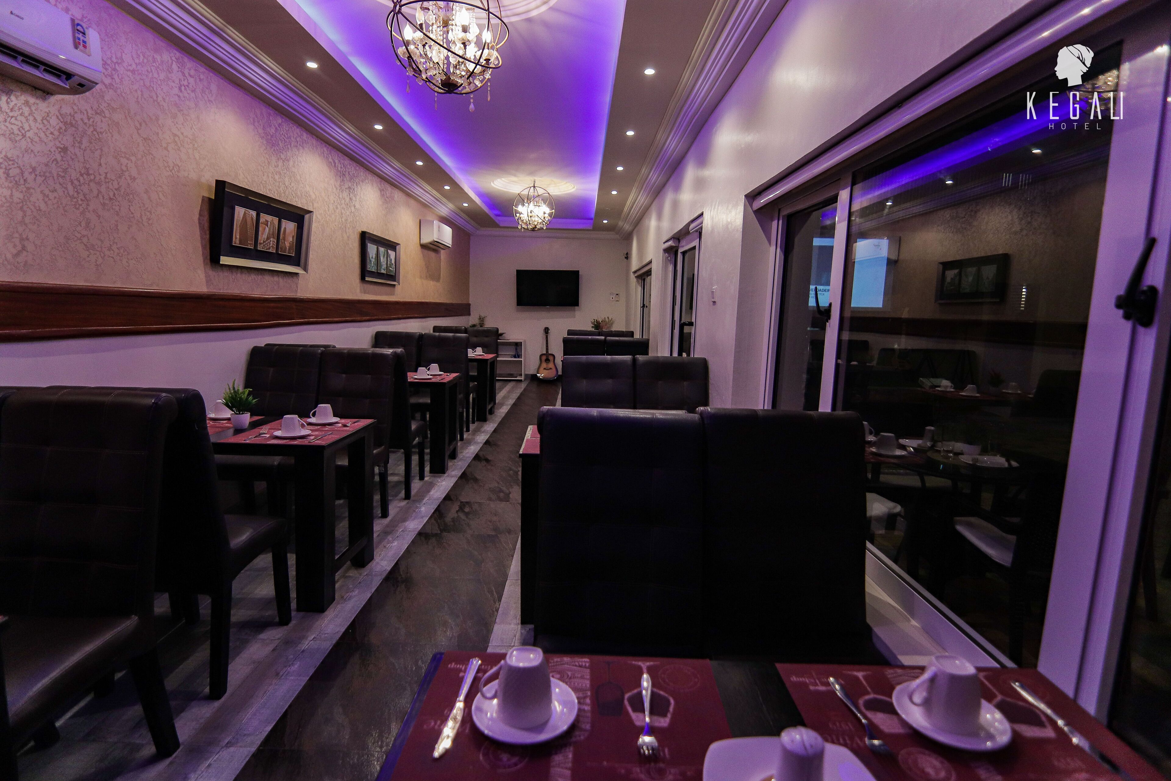 A dimly lit restaurant with tables set for dining, a television mounted on the wall, and a chandelier.