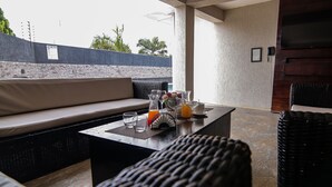 A sunlit outdoor seating area with a cushioned bench, a table with drinks and glasses, and a view of the cityscape. - Kegali Hotel (Accra)