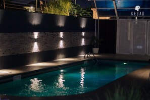 A swimming pool with a brick wall and a metal fence, illuminated by wall-mounted lights. - Kegali Hotel (Accra)