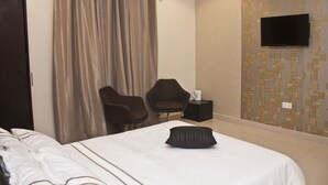 A hotel room with a bed, two chairs, a flat-screen TV, and a wall-mounted air conditioner. - Kegali Hotel (Accra)