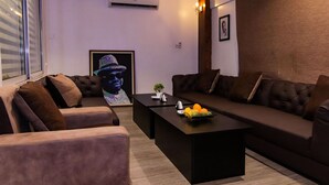 A modern living room with a sofa, armchairs, a coffee table, and a framed artwork on the wall. - Kegali Hotel (Accra)