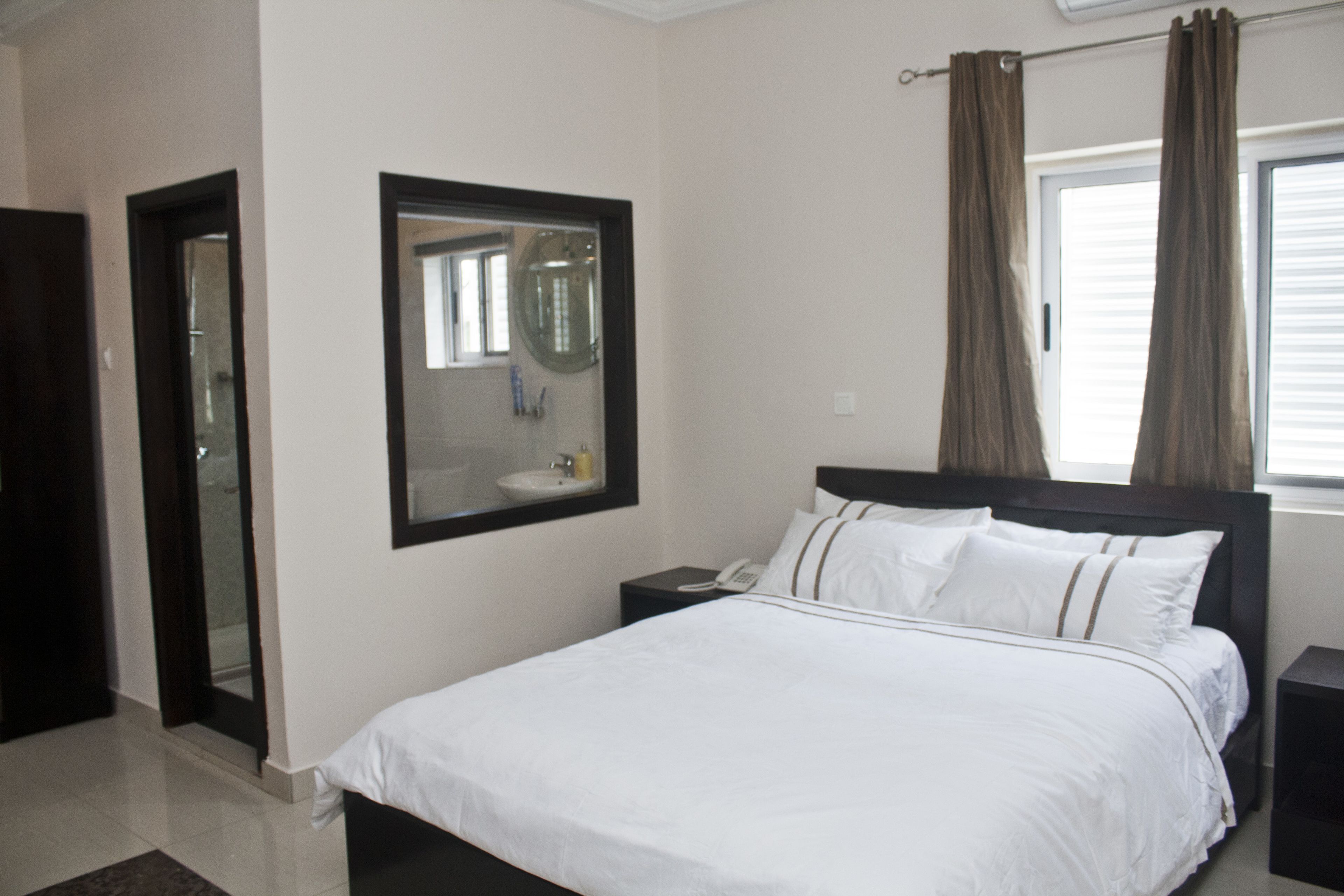 Een hotelkamer met een bed, nachtkastje, spiegel en raam met gordijnen.
