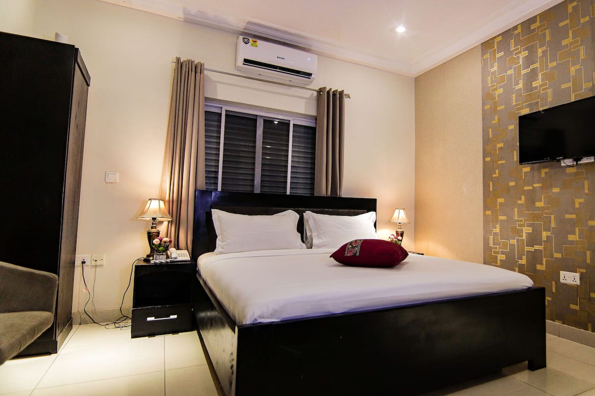 Habitación de hotel con una cama, dos mesitas de noche con lámparas, un equipo de aire acondicionado, un televisor y una pared con diseño.