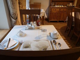 Una mesa de comedor puesta con mantel blanco, platos, cubiertos y copas. Hay botellas de salsas y condimentos sobre la mesa.