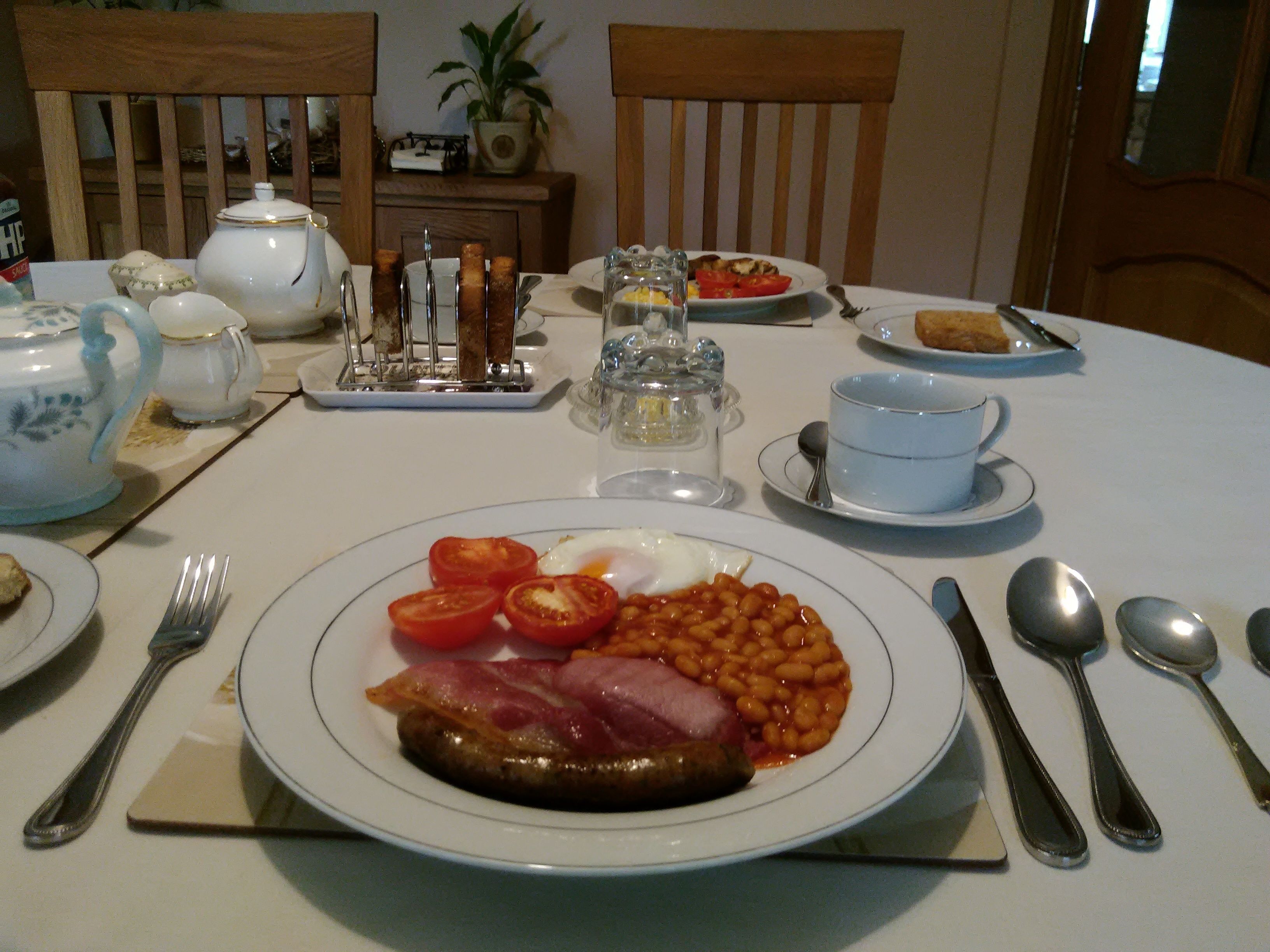 A dining table set with plates of food, cutlery, and a teapot.