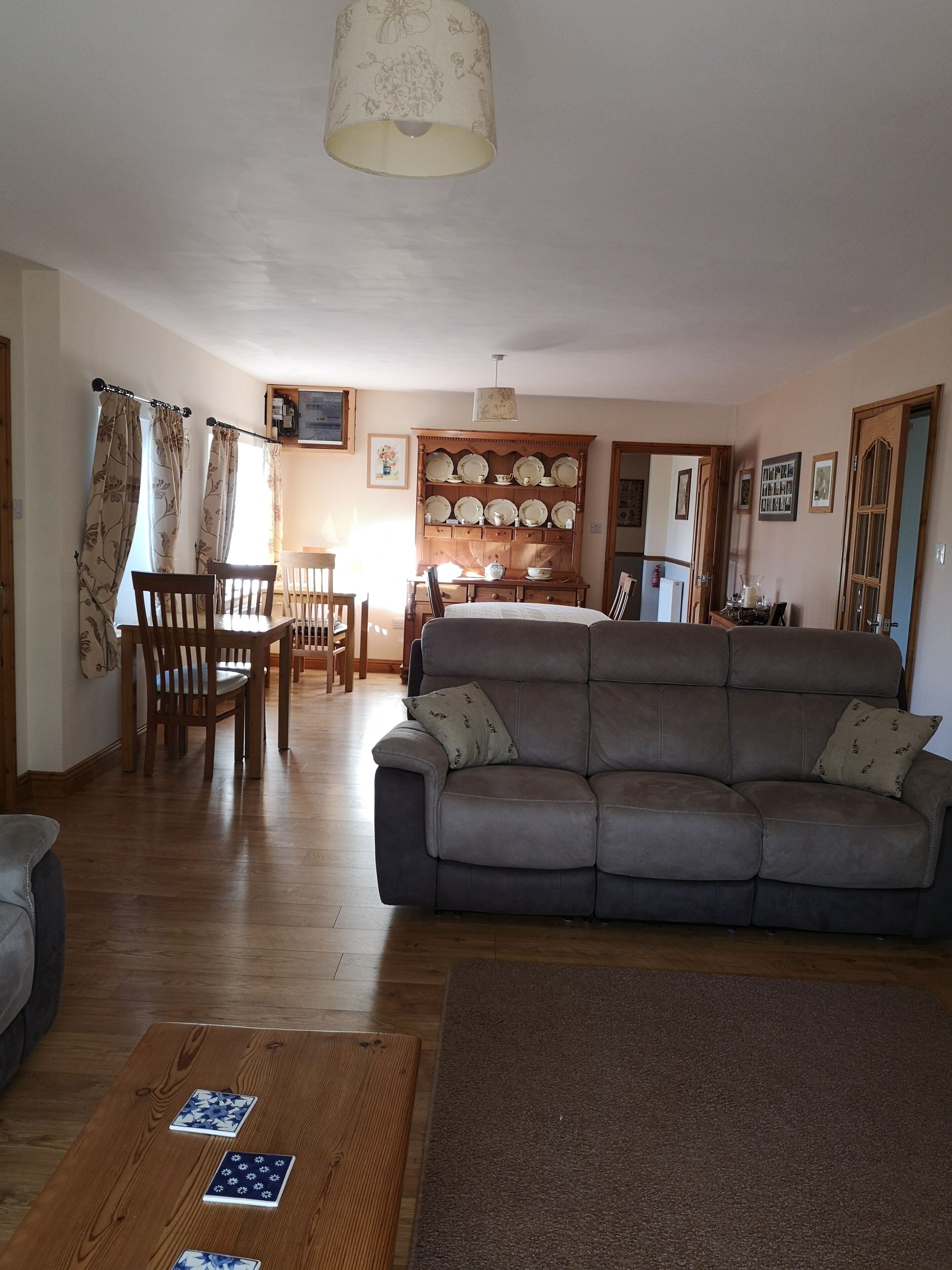 A living room with a sofa, wooden chairs, a dining table, and a wall-mounted plate rack.