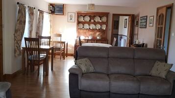 A living room with a sofa, wooden chairs, a dining table, and a wall-mounted plate rack.