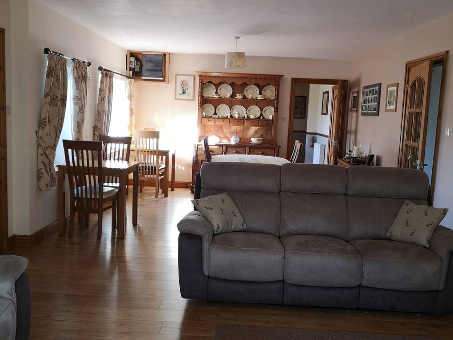 A living room with a sofa, wooden chairs, a dining table, and a wall-mounted plate rack.