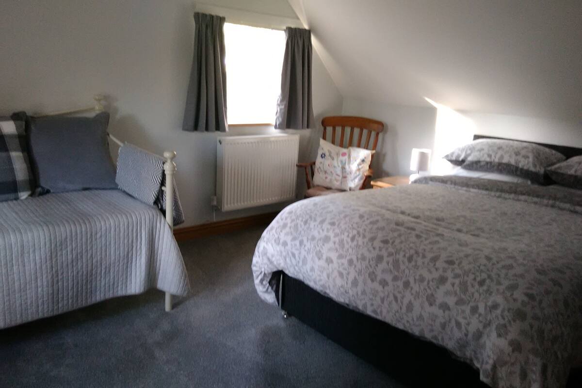 A bedroom with two beds, a radiator, a window with curtains, and a wooden headboard.