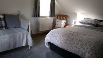 A bedroom with two beds, a radiator, a window with curtains, and a wooden headboard.