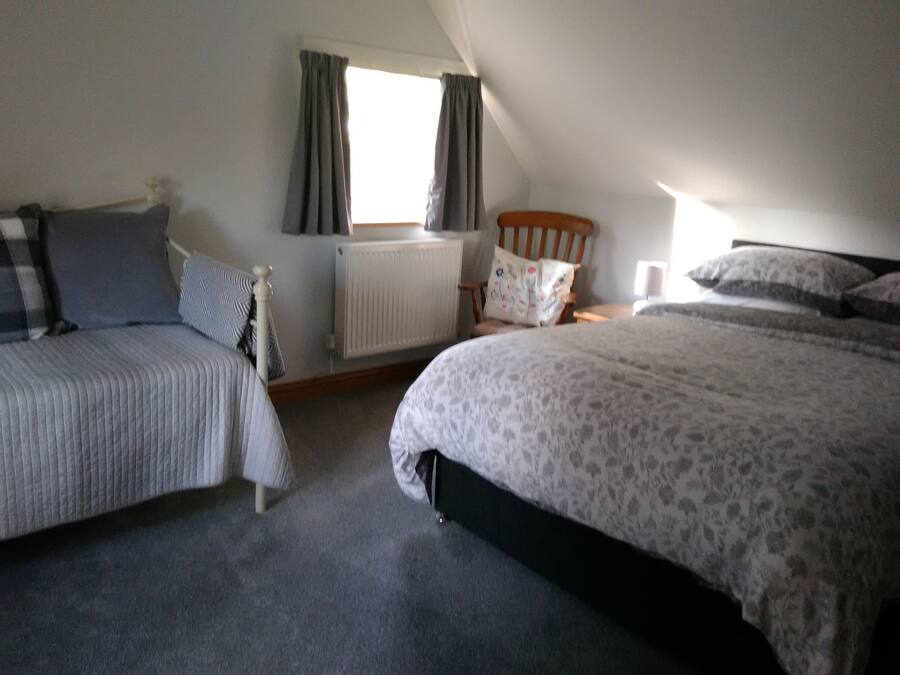 A bedroom with two beds, a radiator, a window with curtains, and a wooden headboard.