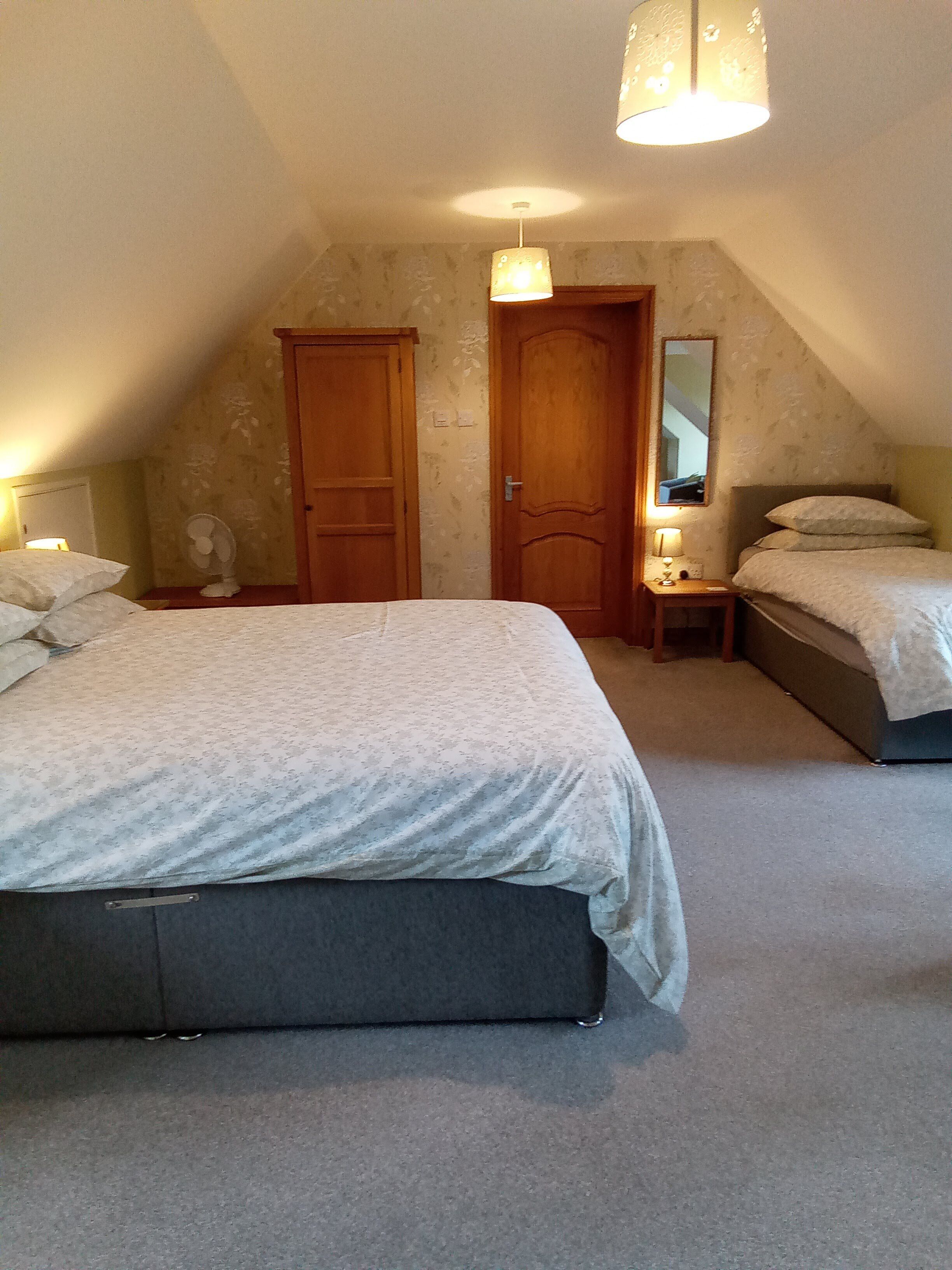 A bedroom with a large bed, two bedside tables, a mirror, and a ceiling fan.