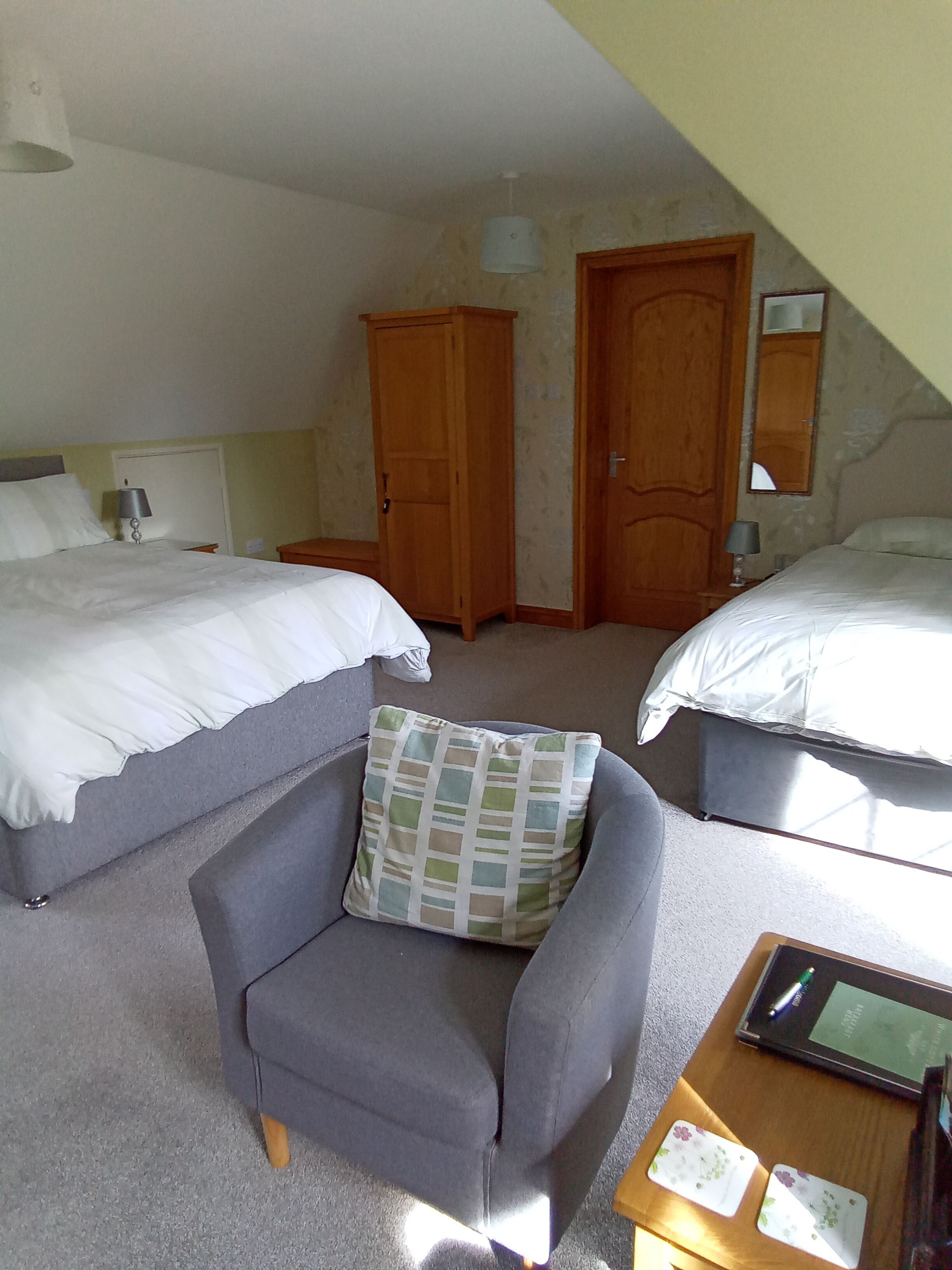 A bedroom with two beds, a chair, a bedside table with a lamp, and a wardrobe.