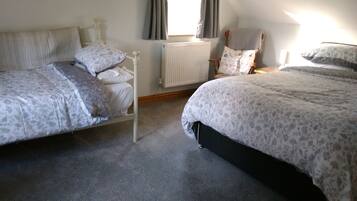 Ein Schlafzimmer mit zwei Einzelbetten, einem Heizkörper, einem Fenster mit Vorhängen und einem Sessel mit Kopfkissen.