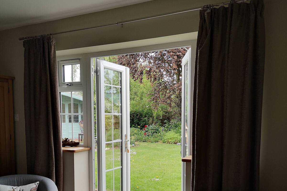 A living room with two grey armchairs, a small wooden table, and a sliding glass door leading to a garden.