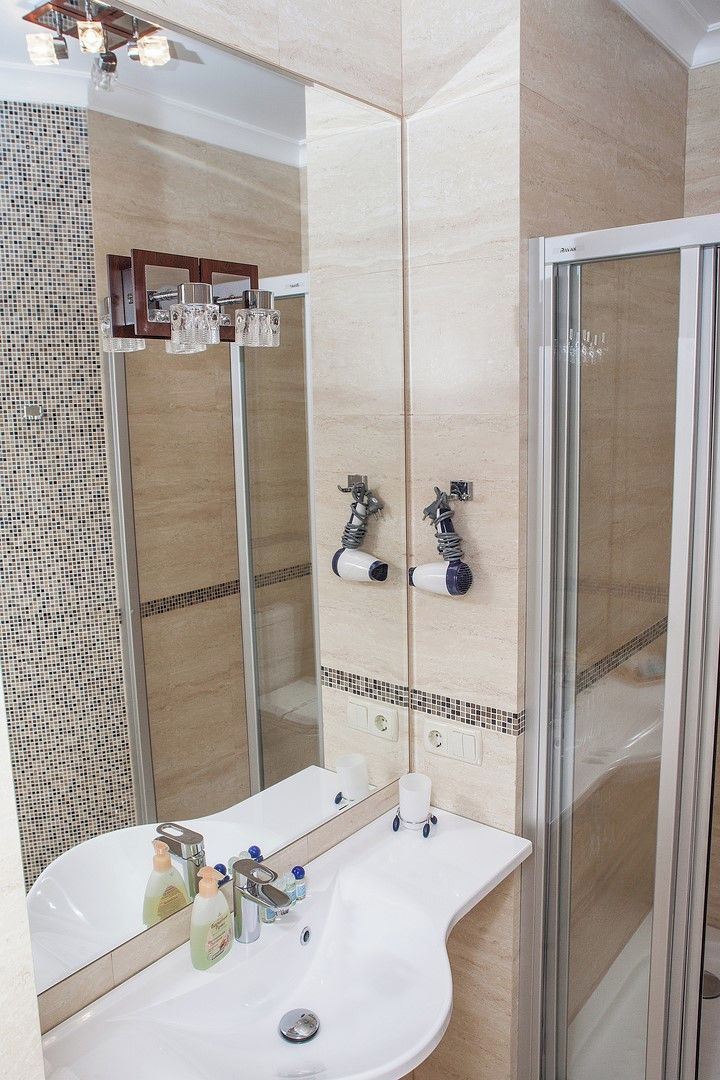 Un baño moderno con cabina de ducha de vidrio, un lavamanos blanco con múltiples grifos y un espejo con detalles de azulejos decorativos.