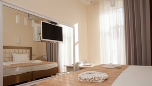Habitación de hotel con una cama grande, un televisor montado en la pared, una mesita de noche y una ventana con cortinas.