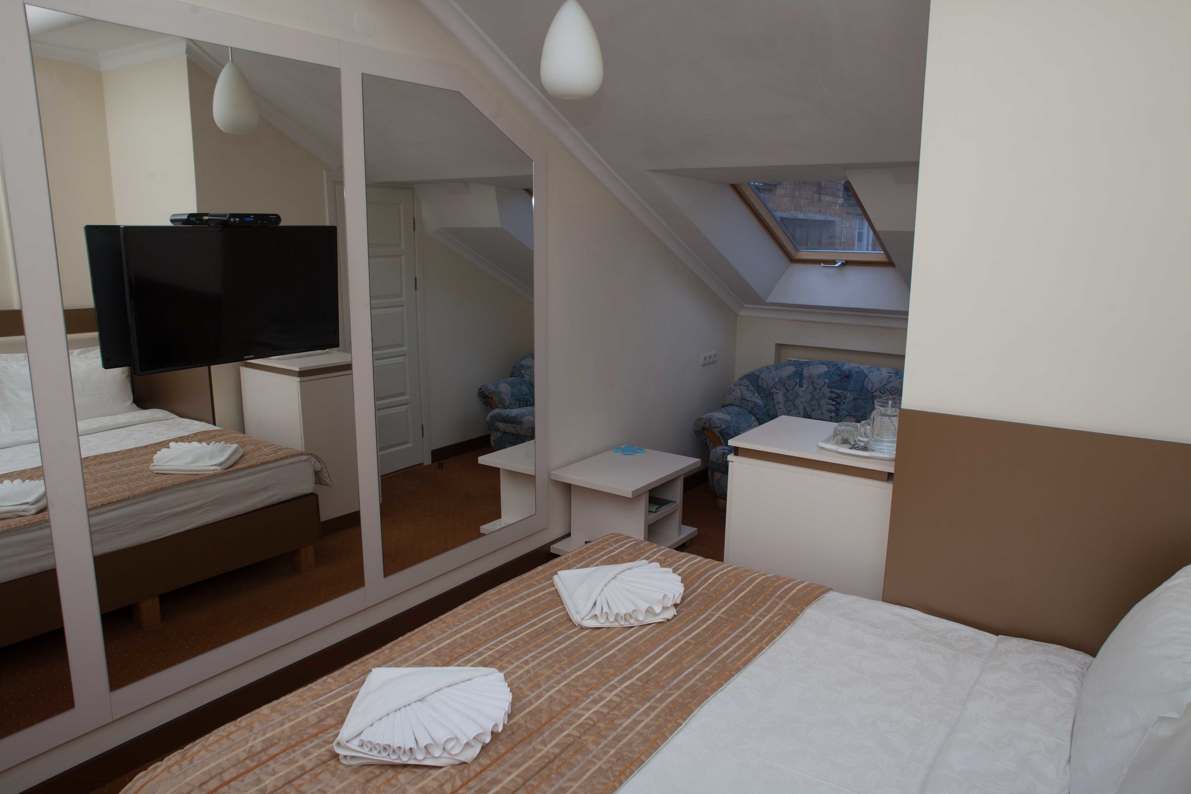 Une chambre d’hôtel avec un lit, une télévision, une petite table et une salle de bain visible à travers un miroir.