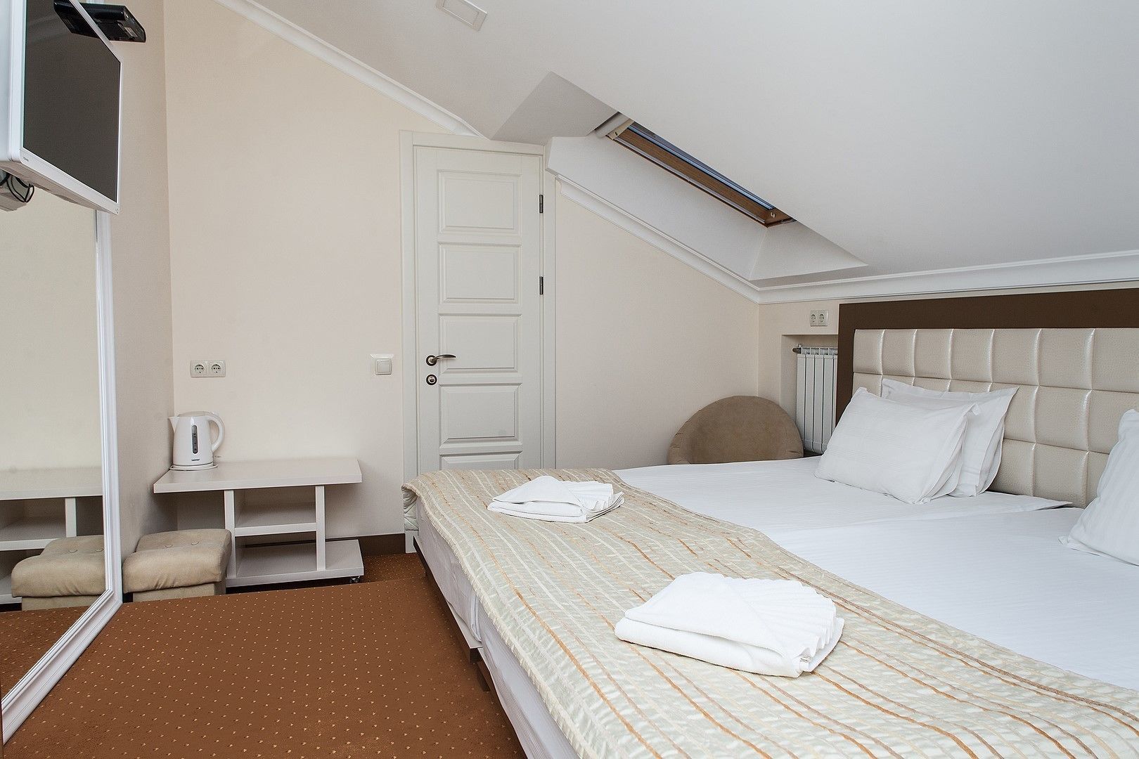 A hotel room with a bed, a bedside table, a chair, a mirror, and a door.