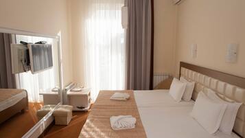 A hotel room with a large bed, a bedside table, a mirror, and a window with curtains.