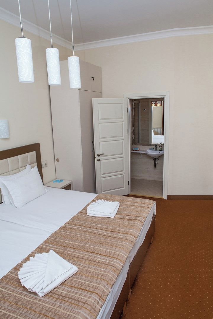 Une chambre d’hôtel comprenant un lit, une table de chevet, une salle de bain avec un lavabo et un miroir, et une porte donnant sur une autre pièce.