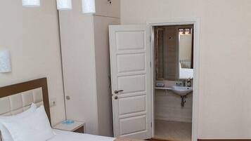 Une chambre d’hôtel comprenant un lit, une table de chevet, une salle de bain avec un lavabo et un miroir, et une porte donnant sur une autre pièce.