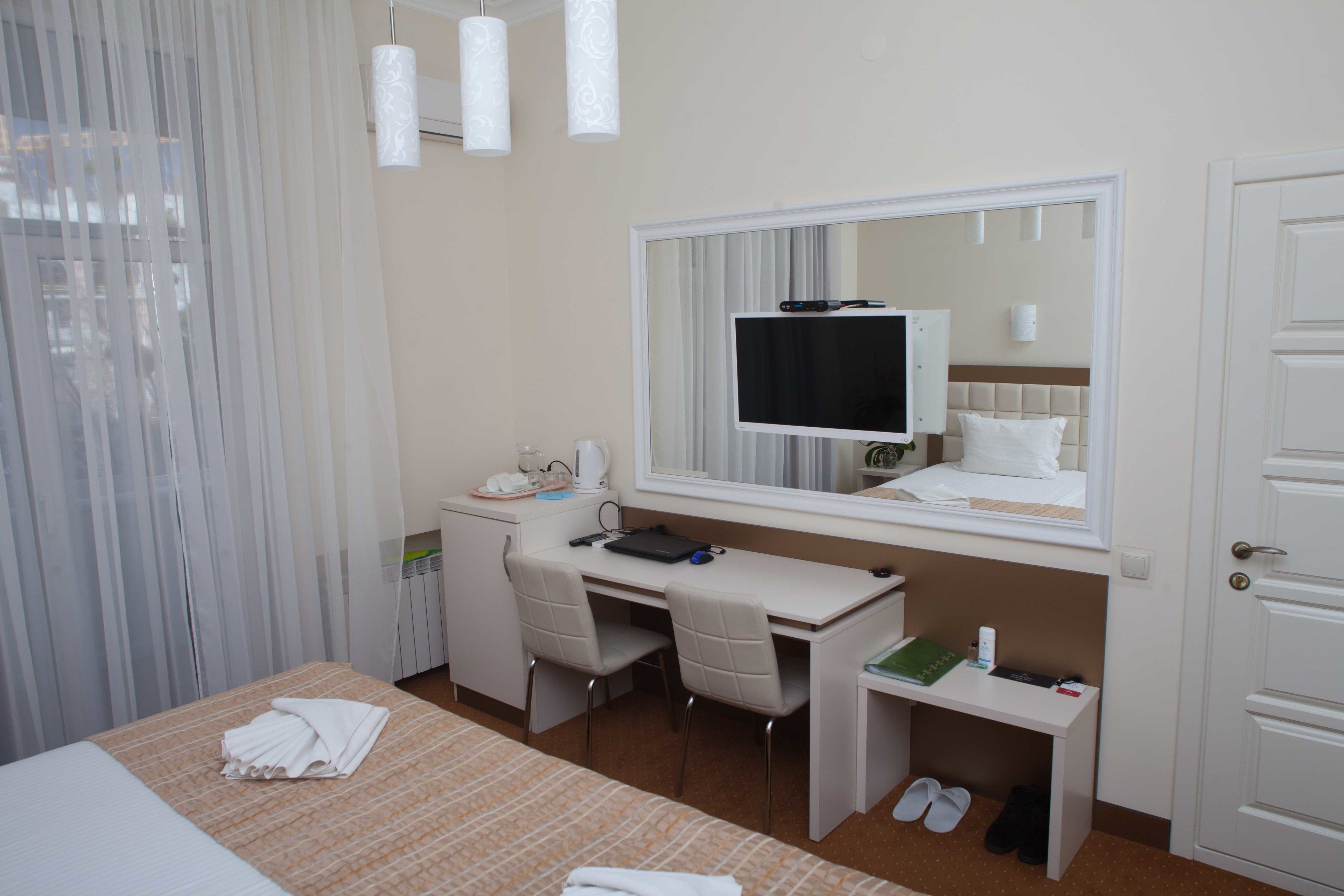 Ein Hotelzimmer mit Bett, Schreibtisch, Stuhl, Fernseher, Spiegel und Tür.