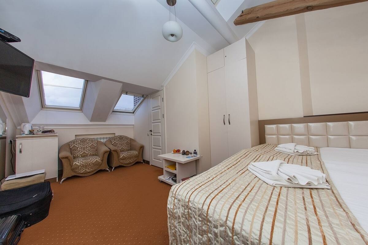 Habitación de hotel compacta con cama, dos sillones, un escritorio pequeño, armario y tragaluz.