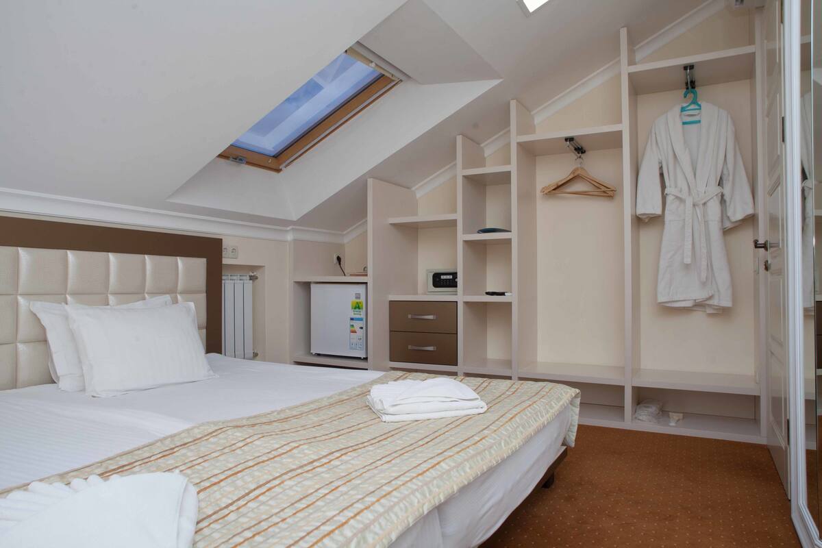 Una habitación de hotel con cama, armario, escritorio, radiador y tragaluz.