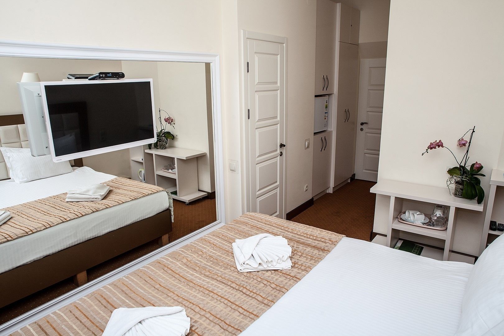 Quarto de hotel com cama, televisão, escrivaninha e guarda-roupa.