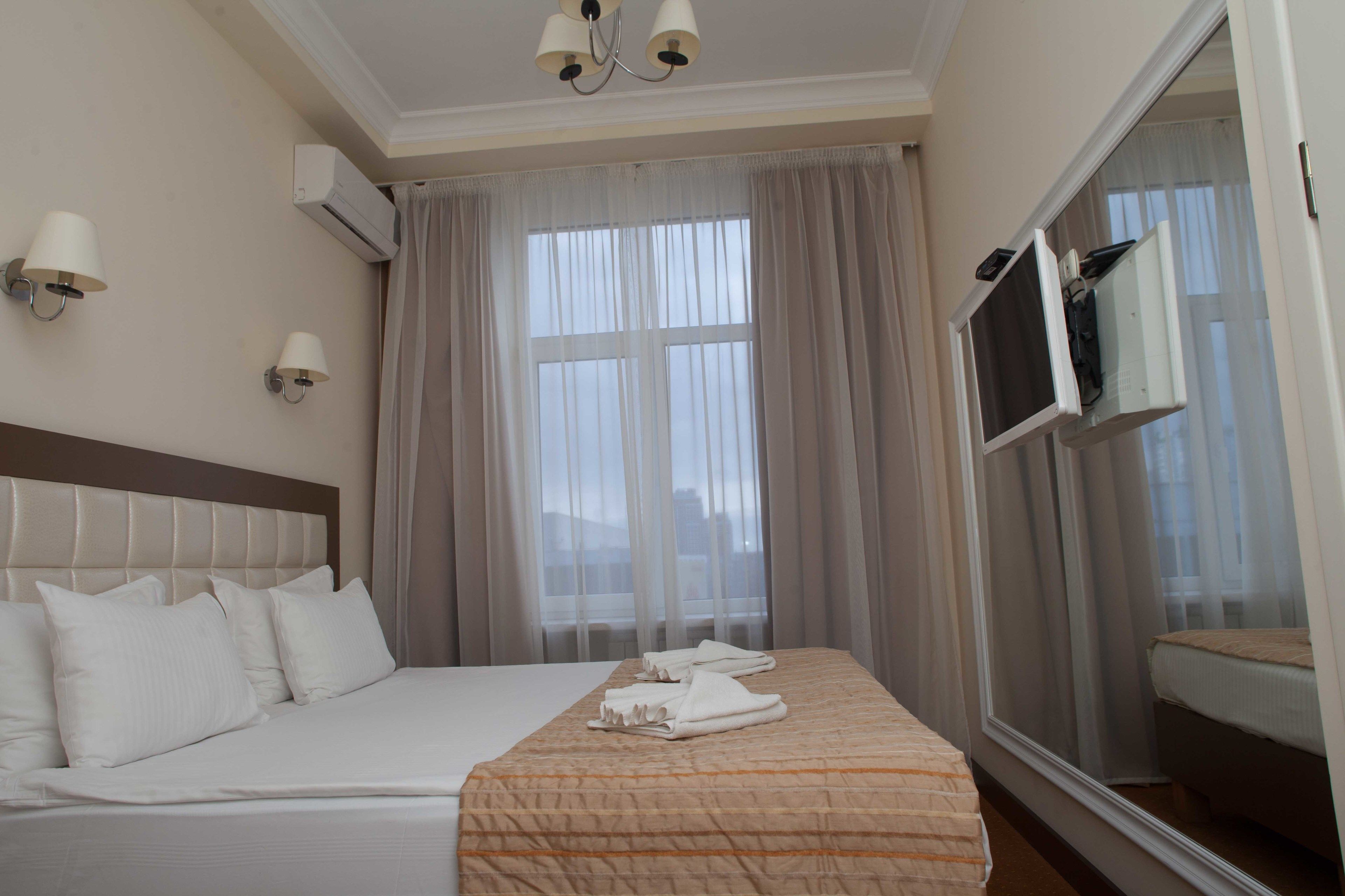 Une chambre d’hôtel avec un grand lit, un téléviseur fixé au mur et une fenêtre avec des rideaux légers.