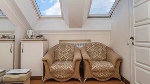 Una habitación con dos tragaluces, un armario blanco, un par de sillones estampados y un ordenador portátil sobre una pequeña mesa.