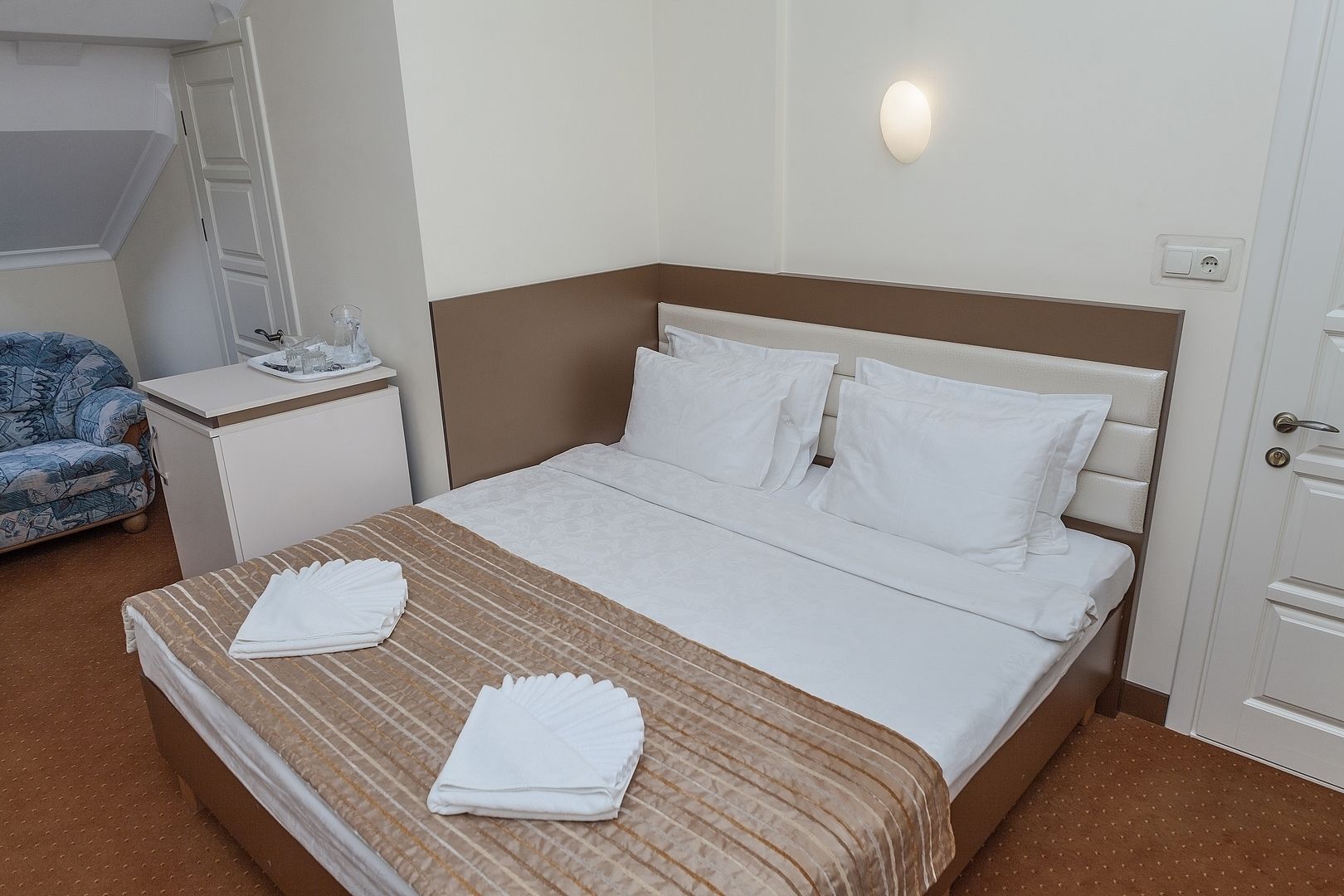 Ein Hotelzimmer mit Bett, Nachttisch, Sessel und Wandleuchte.