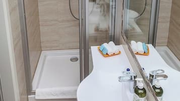 Un baño moderno con ducha de vidrio, un lavamanos blanco con espejo y un perchero para toallas.