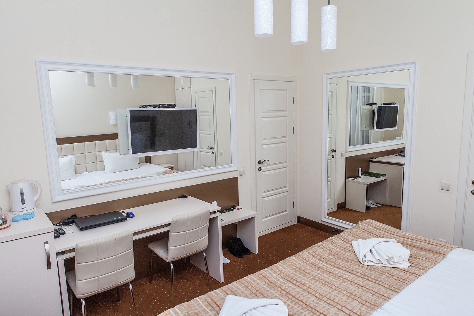 Una habitación de hotel con una cama, un escritorio con computadora, una silla, un espejo y una puerta.