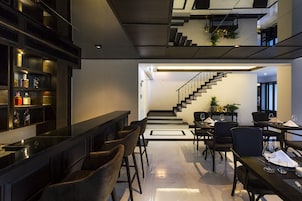 Un interior moderno con una zona de bar, comedor y una escalera que conduce a un nivel superior.