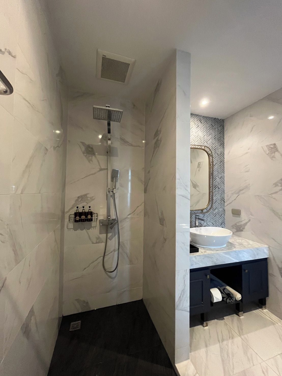 Un baño moderno con cabina de ducha, tocador con espejo grande y mueble de color oscuro.