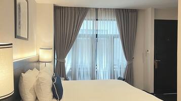 Una habitación de hotel con una cama grande, una mesita de noche con lámpara y una ventana con cortinas.