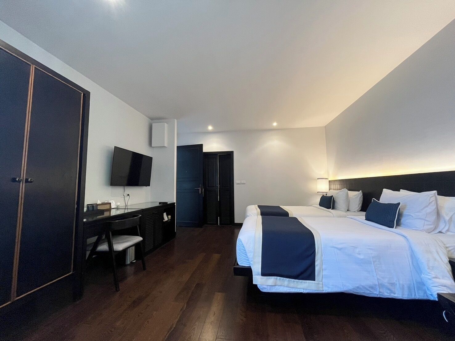 A modern hotel room with a large bed, a desk with a chair, a television, and a wardrobe.